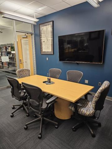 Meeting room with a table, 6 chairs, and a display screen on the wall